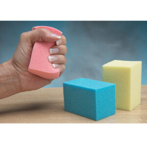 Hand squeezing a pink sponge with two other sponges on a table.